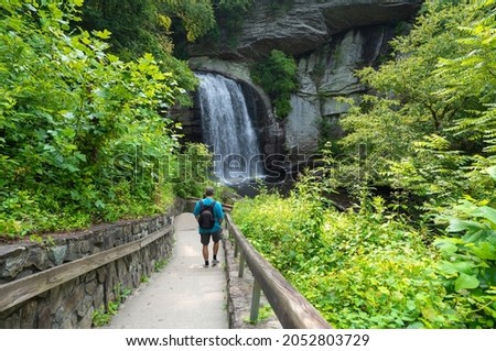 Man hiking in the forest. Hiker with backpack walking on the path  to the waterfall. Looking Glass Falls near Brevard, Pisgah National Forest, North Carolina, USA. 