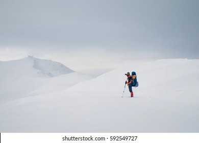 Man Hiking On Snow Hills With Trekking Sticks And Snowshoes Over The Clouds. Winter Sport Activity. View From The Back Side