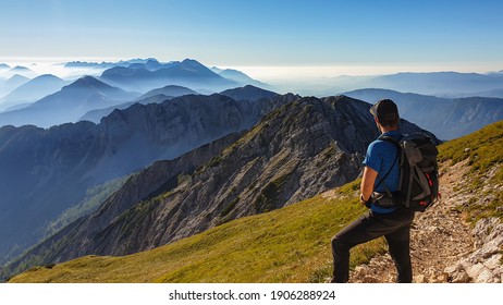 A man in a hiking outfit with a panoramic view on the haze shrouded valley from the way to Mittagskogel in Austrian Alps. Clear and sunny day. Endless mountain chains. Outdoor activity. Achievement