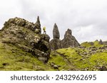 Man hiking in Scotland, Isle of Skye at the Old Man of Storr - Hiker climbing on rocks with the famous rock of the Isle of Skye on a cloudy  day - Travel and adventure concepts