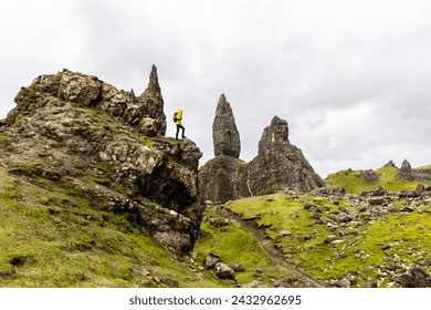 Man hiking in Scotland, Isle of Skye at the Old Man of Storr - Hiker climbing on rocks with the famous rock of the Isle of Skye on a cloudy  day - Travel and adventure concepts - Powered by Shutterstock