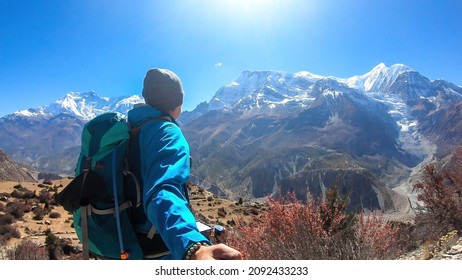A man hiking and taking a selfie with snow caped Annapurna chain in the back, Annapurna Circuit Trek, Himalayas, Nepal. High mountains around. The man is admiring the landscape. Serenity and calmness.