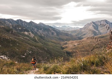 Man Hiking Towards Valley On A Trail With A Brown Hiking Backpack And Orange Tent On His Back In The Witfontein Nature Reserve In Western Cape.