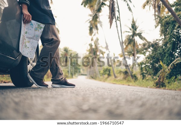 A man with and\
him lost on the road and hold map side a car on the road in forest.\
Backpack travel concept.