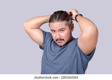 A Man In His 30s Ties His Long Hair Into A Ponytail With An Elastic Band. A Guy In A Gray Shirt Fixing His Messy Hair. Isolated On A Gray Background.