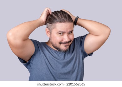 A Man In His 30s Ties His Long Hair Into A Ponytail With An Elastic Band. A Guy In A Gray Shirt Fixing His Messy Hair. Isolated On A Gray Background.