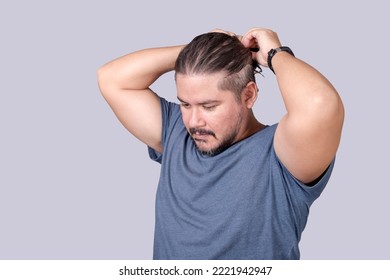 A Man In His 30s Ties His Long Hair Into A Ponytail With An Elastic Band. A Guy In A Gray Shirt Fixing His Messy Hair. Isolated On A Gray Background.