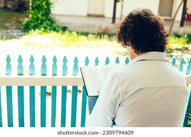 A man with his back is reading a book on the veranda. Peace in the countryside - Powered by Shutterstock