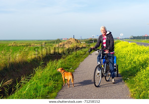 Man with his\
dog at the bike in Dutch\
landscape