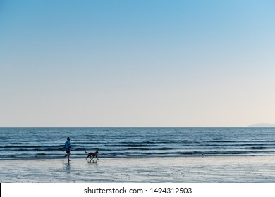 A Man And His Dog Take An Early Evening Walk Along The Seashore