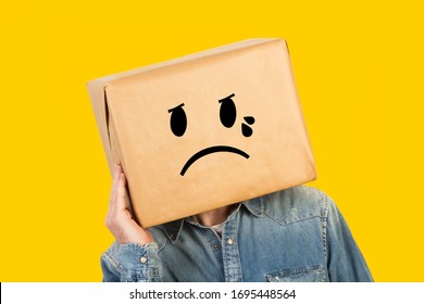 Man with his head in a box and crying gesture drawn on it and on a yellow background