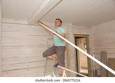 A Man In His House Installs A Wooden Plinth On The Ceiling