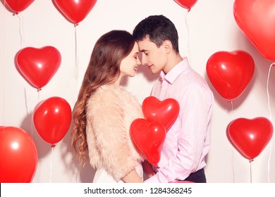 Man with his lovely sweetheart girl kiss at Lover's valentine day. Valentine Couple. Couple kiss and hug. On background red balloons hearts. Love concept. Happy smile girl. Lovers touch foreheads 