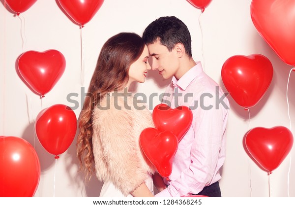 恋人のバレンタインデーに 愛らしい恋人の女の子のキスをした男性 バレンタインカップル カップルのキスとハグ 背景に赤い風船のハート 愛のコンセプト 幸せな笑顔の女の子 恋人は人の顔に触れる の写真素材 今すぐ編集
