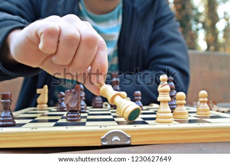 A man in his mid-twenties sits in an autumnal park and plays chess - focusing on the game pieces on the board, the person can not be seen and only the hands and torso are visible