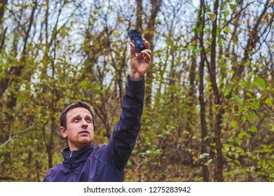 Man With His Mobile Smart Phone Searching For Reception Signal In The Forest.