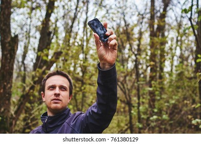 Man With His Mobile Smart Phone Searching For Reception Signal In The Forest.