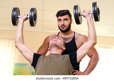 Man And His Personal Trainer Exercising With Dumbbells At The Gym. Technique Exercises For The Shoulders. Novice Athlete With Coach