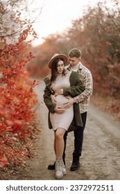 A man and his pregnant wife are walking in an autumn park, spending time together. Concept of love, relaxation, people. Active lifestyle.