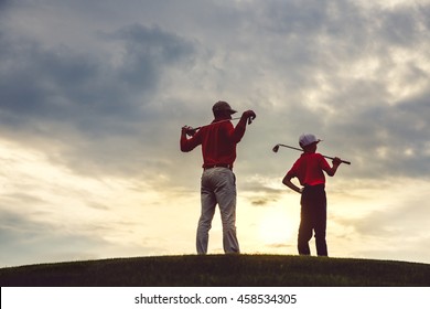 man with his son golfers standing on golf course at sunset, back view