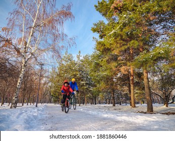 A Man And His Son Ride Bicycles In The City Park In Winter. An Active Family Weekend On A Sunny Winter Day