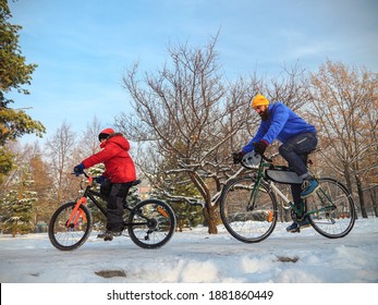 A Man And His Son Ride Bicycles In The City Park In Winter. An Active Family Weekend On A Sunny Winter Day