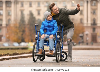 Man with his son in wheelchair taking selfie outdoors on autumn day