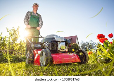 Man in his sunny garden mowing the grass with a lawn mower - Shutterstock ID 1708981768