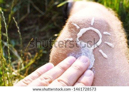 A man in his twenties lies in a meadow and has painted a sun with sunscreen on his right knee - the focus is on his right knee - Sun protection concept in the hot summer