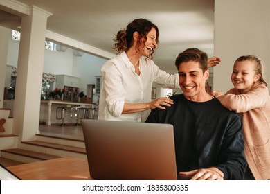 Man with his wife and daughter sitting in front of laptop making a video call. Happy family making video call while at home. - Powered by Shutterstock