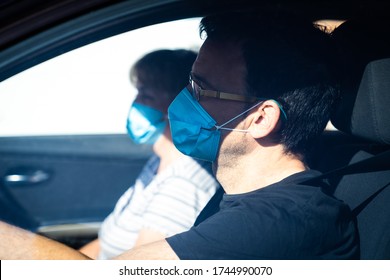 Man With His Wife On Background Wearing Protective Mask Driving. Mature Couple Driving In The Car With Face Mask.