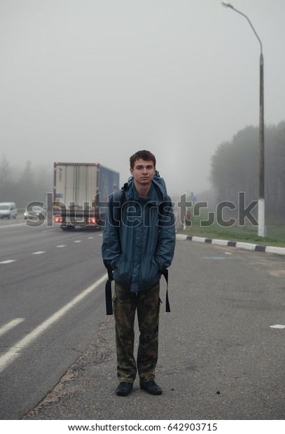 Man\
hitchhiking on the highway in the foggy\
morning