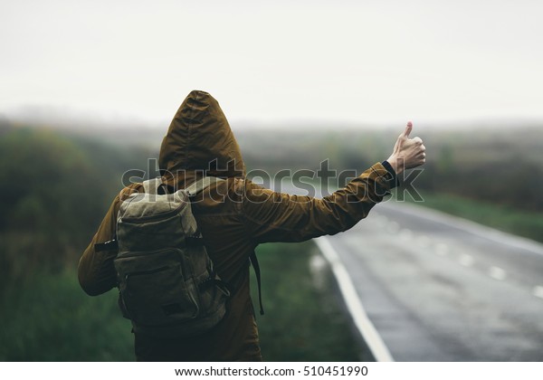Man hitchhiking on road\
in autumn fog