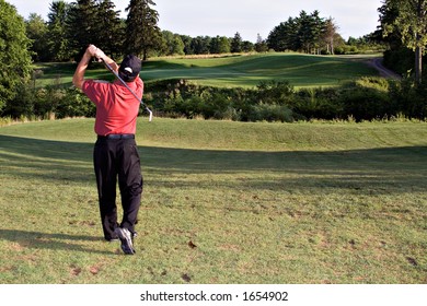 Man Hitting A Long Drive Toward The Distant Green Ahead.  Beautiful Landscape View Of Golf Course.