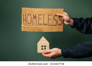 A man hold a cardboard house and sign with the inscription HOMELESS. Dark background. Hands close-up. The concept of helping vagabonds.