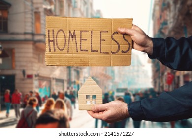 A man hold a cardboard house and sign with the inscription HOMELESS. Dark background. Hands close-up. The concept of helping vagabonds