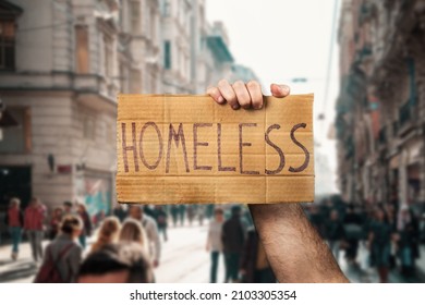 A man hold a cardboard sign with the inscription HOMELESS. Defocused background with street and people. Hands close-up. The concept of helping vagabonds.