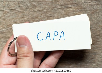 Man hold the flash card with handwriting word CAPA (abbreviation of corrective action and preventive action) on wood background