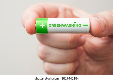 Man Hold A Green And White Battery With The Word Greenwashing Printed On It. Greenwashing Is A Communication Technique Aimed At Building A False Image Of A Company In Terms Of Environmental Impact.