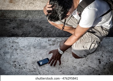 man hold the head with hand and grab a broken smartphone with crashed screen on the concrete floor.