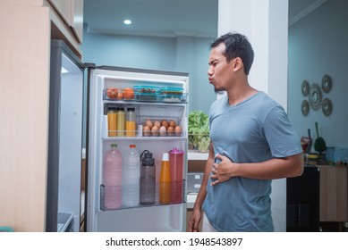 Man Hold His Belly While Open The Fridge Door Looking Something To Eat