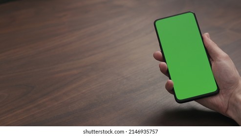 Man Hold Smartphone With Greenscreen On Walnut Table, Wide Photo