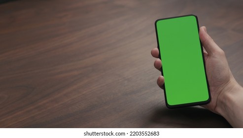 Man Hold Smartphone With Greenscreen On Walnut Table, Wide Photo