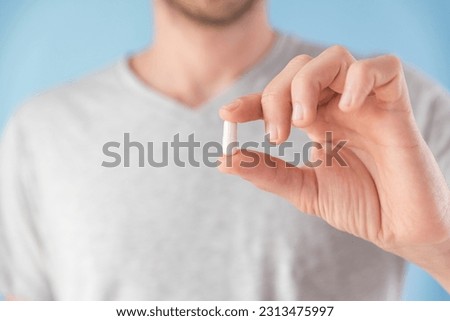 Man hold white capsule with collagen in male hand on blue background. Nutritional supplement, medicine, drug for joints protection, skin care, arthritis prevention