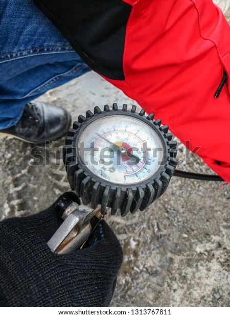 The man is holding an air pump with a a\
pressure gauge for inflating car\
tires