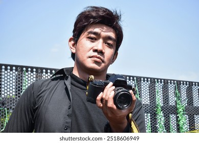 a man is holding an analog camera with a sharp gaze.