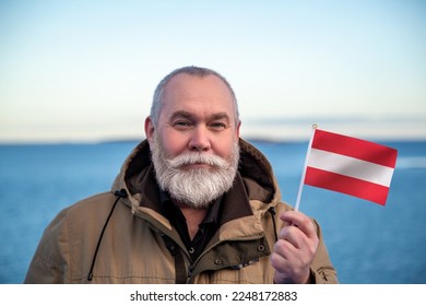 Man holding Austria flag. Portrait of older man with a national Austrian flag. Visit Austria concept. Older man 50 55 60 years old with gray beard outdoors travelling in winter. Travel to Austria