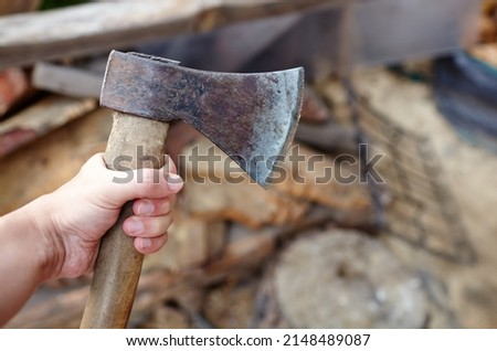 Man holding axe. Ax in hand. A strong man holds an ax in his hands against the background of firewood. Selective focus, blurred background