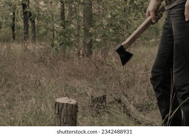 A man is holding an axe. The photo shows the legs and arms of a man. Male mysterious portrait in the forest. Vintage photo.
