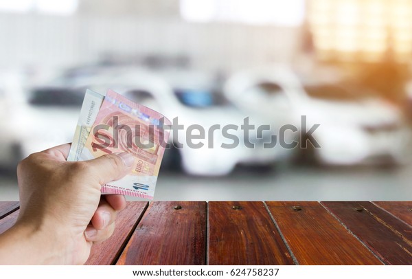 Man holding a banknote , blur image of white\
cars as background.